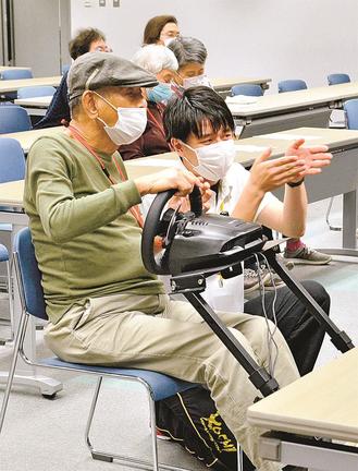 島根大生（右）から説明を受けながらｅスポーツを体験する高齢者（左）＝松江市朝日町、松江テルサ