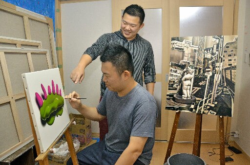 作品を描く兄の木原幸志郎さん(手前)にアドバイスする木原健志郎さん=広島県尾道市内