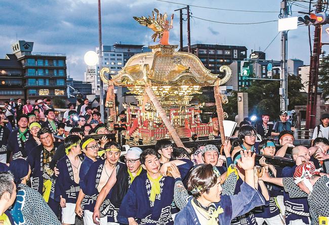 本宮を担ぎ、まちを練り歩く男性たち＝２４日午後７時半、松江市白潟本町、松江大橋南詰め