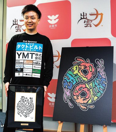 「出雲神話まつり」のロゴを披露し、原画を手にする久保和稀さん＝出雲市今市町、市役所