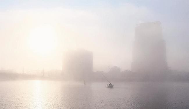 朝霧を太陽が照らし、ビルや漁師の影が浮かび上がる大橋川周辺＝４日午前７時５９分、松江市末次本町