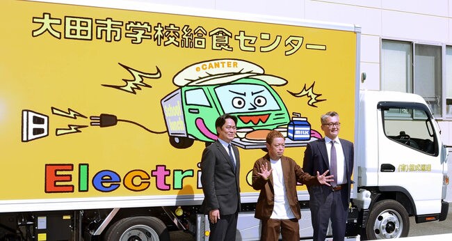 「バキバキ画」が描かれた給食運搬用のＥＶトラックの前でポーズを取るネゴシックスさん（中央）＝大田市川合町、市学校給食センター