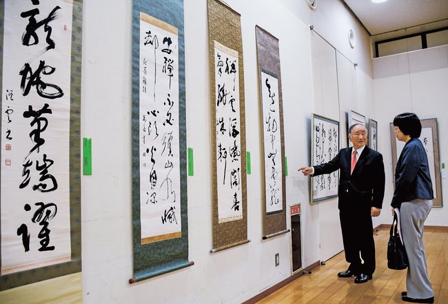 出雲書道会歴代会長の作品を来場者に解説する若槻十鴻会長（左）＝出雲市浜町、縁結び交流館