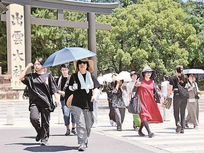 出雲大社前で日傘を差し、帽子姿で歩く観光客＝出雲市大社町杵築南