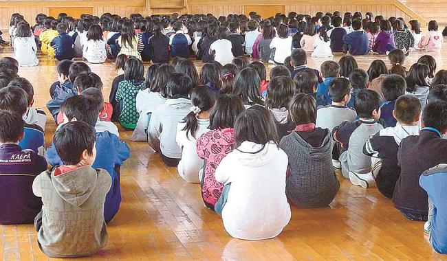 集会で体育館の床に「体育座り」する子どもたち（資料）