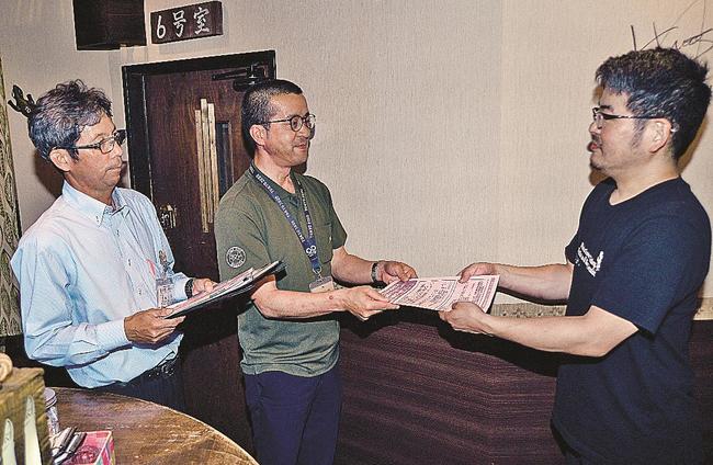 松本英次さん（右）にチラシを手渡す潮信次所長と豊田芳明事務局長＝益田市駅前町、すずめのがっこう
