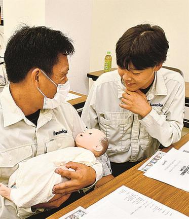 生後間もない赤ちゃんの人形を抱いて、笑顔を見せる社員たち＝出雲市塩冶神前２丁目、今岡工業