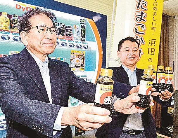 自販機の前で商品を手にするマルハマ食品の浜崎修司社長（左）＝浜田市殿町、市役所