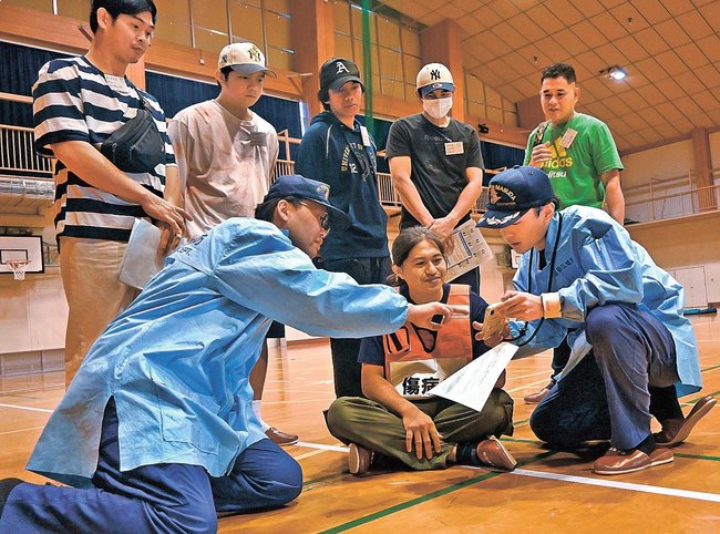 訓練で消防職員に症状を伝える外国人住民（手前中央）＝島根県吉賀町六日市、町民六日市体育館