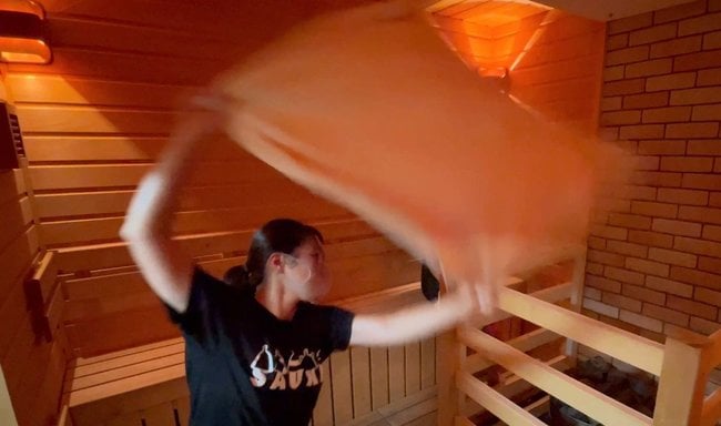 タオルで室内の熱気や蒸気を循環させる、熱波師の五塔熱子（ごとうねつこ）さん＝鳥取県琴浦町野井倉、ネイチャーサウナ
