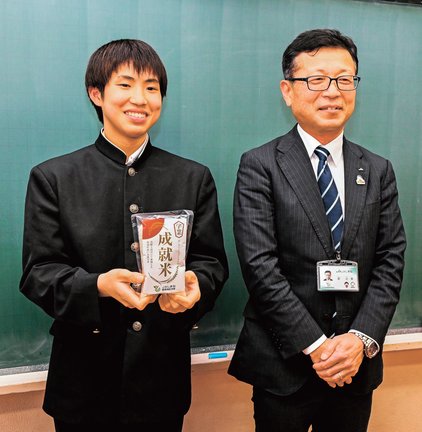 源之美本部長(右)から贈られた「学業成就米」を手にする生徒代表の明見廣惺さん=島根県飯南町下赤名、赤来中学校