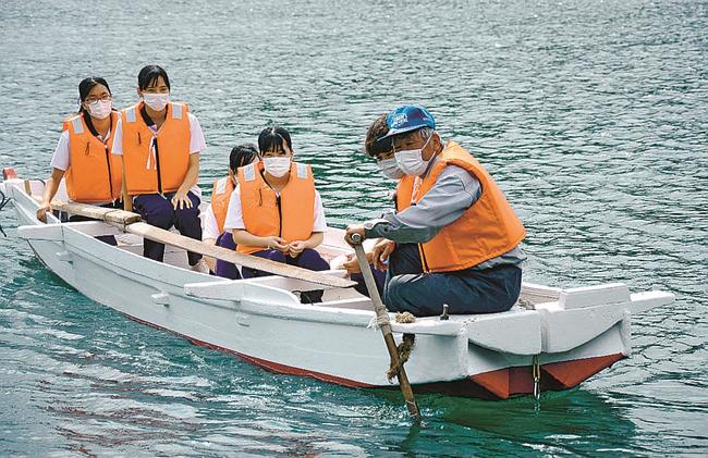 修復したかんこ舟に乗り込み、柏原実さん（右端）から櫂の使い方を教わる隠岐島前高校３年生＝島根県海士町宇受賀、宇受賀漁港内