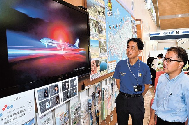 モニター画面に映し出された航空写真を見る有田学さん（右）＝益田市内田町、石見空港ターミナルビル