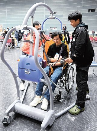 要介護者を車椅子に移動するリフトの操作を体験する参加者＝松江市学園南１丁目、くにびきメッセ