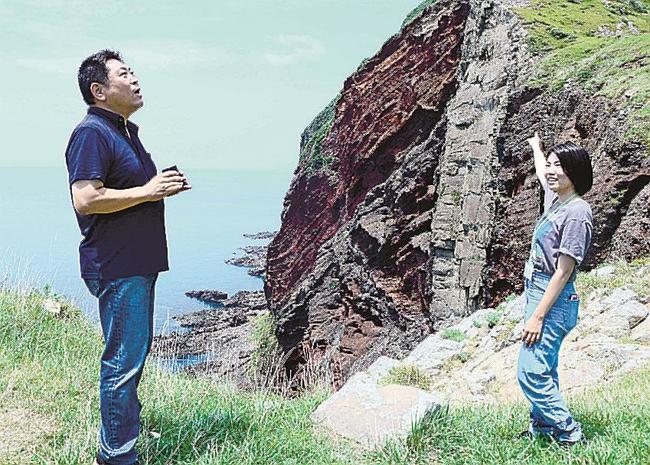 地域おこし協力隊員（右）の案内を受け、赤壁を視察する奥村健太社長＝島根県知夫村