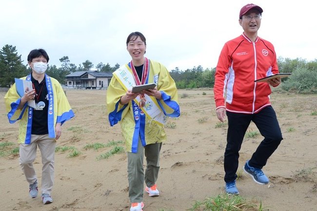 「ポケモンＧＯ」をしながら鳥取砂丘を歩く入江聖奈さん（中央）と平井伸治知事（右）＝鳥取市浜坂