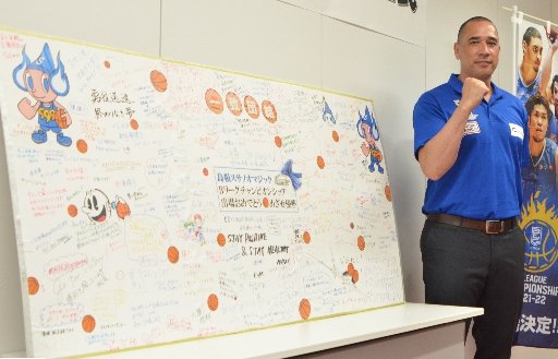 チームに贈られたメッセージボードの横でチャンピオンシップへの意気込みを示すポール・ヘナレ監督＝松江市学園南１丁目、市総合体育館