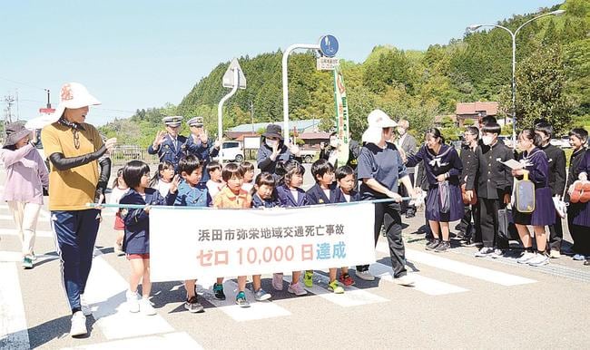 交通死亡事故ゼロ１万日達成の横断幕を持って大通りを歩く園児たち＝浜田市弥栄町長安本郷