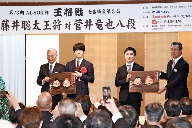 記念品の石見神楽面を受け取る藤井聡太王将（左から２人目）と菅井竜也八段（同３人目）＝大田市三瓶町、国民宿舎さんべ荘