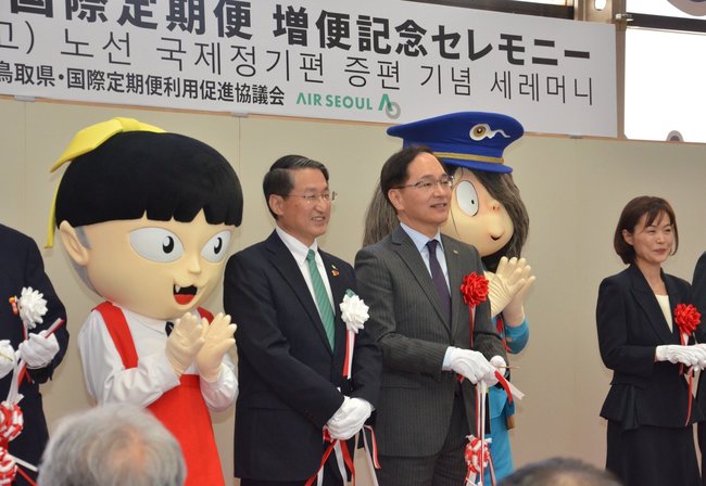 テープカットを終え、笑顔を見せる鳥取県の平井伸治知事（中央左）と、エアソウルの金仲鎬代表理事（同右）＝３月３１日、境港市佐斐神町の米子空港