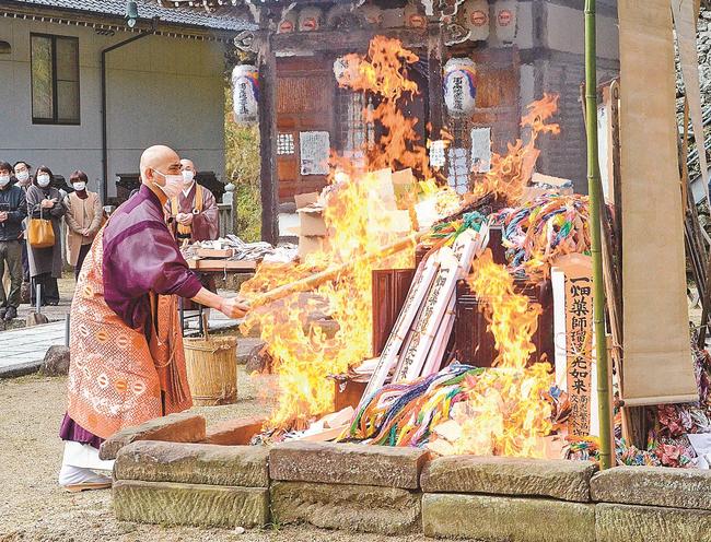 積まれたお札やお守りなどに点火する飯塚大幸管長＝出雲市小境町、一畑薬師