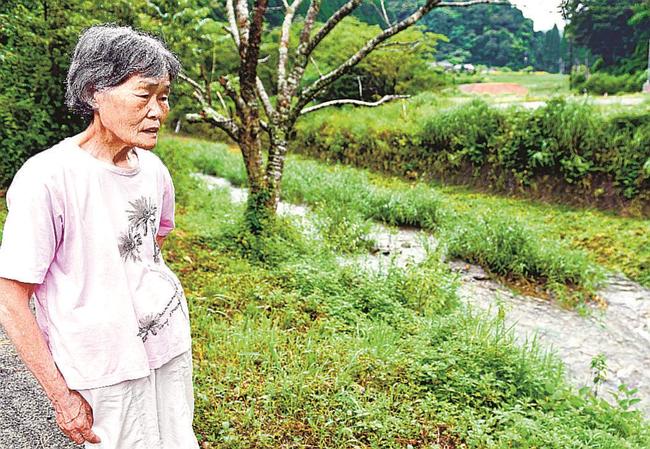 家の前を流れる奥谷川を眺める餅田美代子さん。小さな川は、豪雨になると一気に増水して牙をむく=江津市川平町