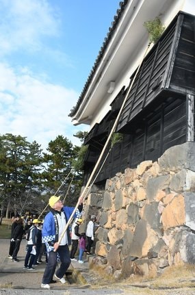 すす梵天を使い、松江城の外壁をきれいにする参加者＝松江市殿町