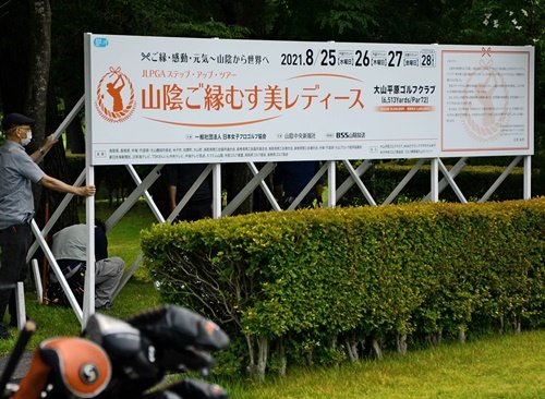 練習グリーン奥に「山陰ご縁むす美レディース」の大型看板を設置する関係者＝鳥取県伯耆町丸山、大山平原ゴルフクラブ