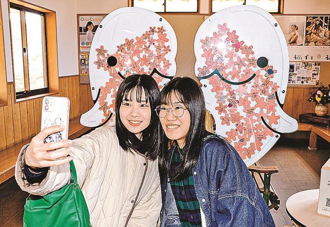 ＪＲ波子駅に設置されたメッセージボードの前で写真を撮る学生＝江津市波子町