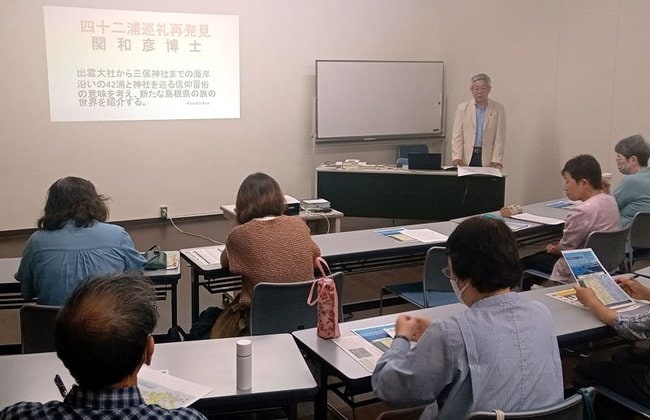 関和彦さんの功績を語る木幡育夫講師（右奥）