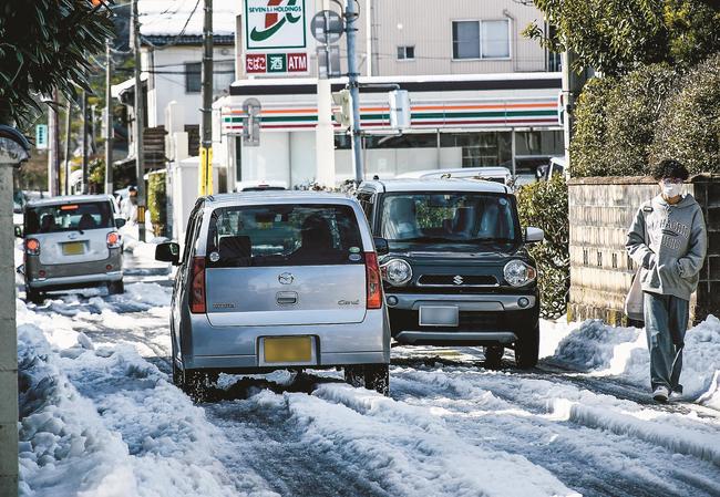残った雪で狭くなった車道を行き交うドライバーと歩行者＝３０日午後２時２分、松江市北田町