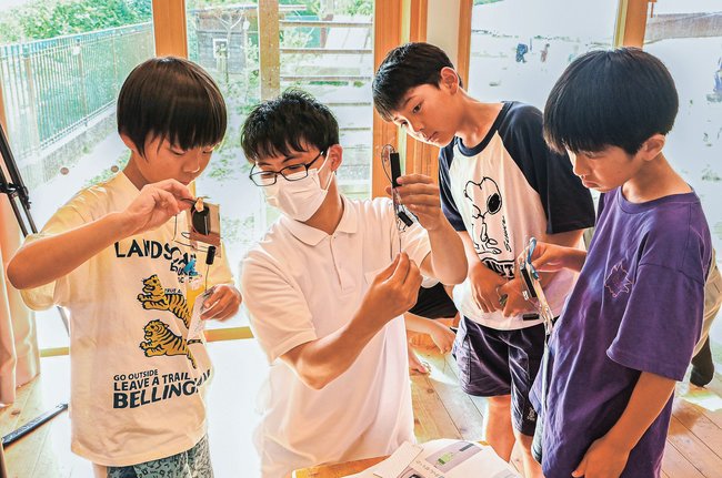 高校生（左から２人目）に教わりながら七夕飾りを作る児童たち＝松江市上乃木８丁目、こばと児童クラブ