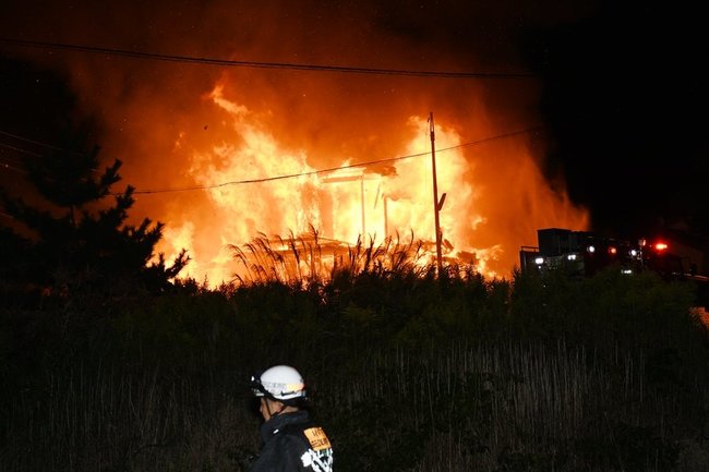 炎を上げる民家と消防士＝11日夜、益田市久城町