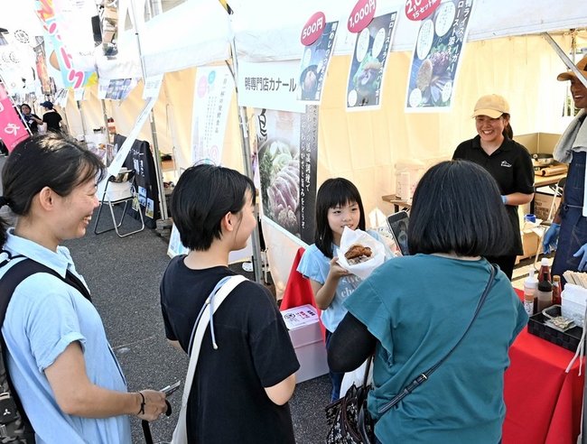 お米を使った創作料理を購入し、記念写真を撮る家族連れ＝松江市学園南１丁目