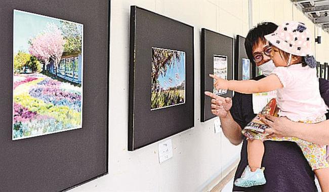 四季の花や風景を写した作品に見入る来場者＝出雲市西新町２丁目、しまね花の郷