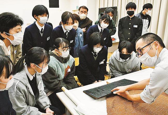 大森拓土専門学芸員（右）に版木を見せてもらいながら、葛飾北斎の解説を受ける生徒たち＝松江市袖師町、島根県立美術館