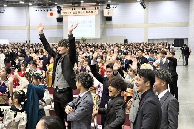 会場の記念撮影でカメラに向かい手を振る出席者