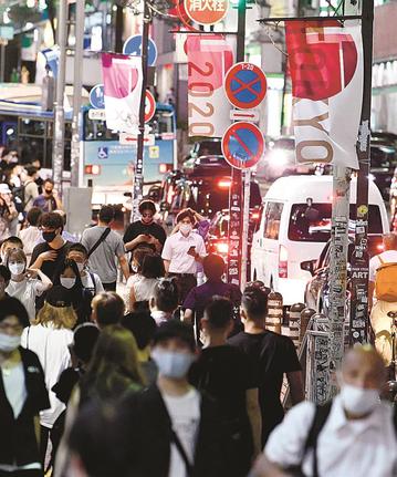 東京五輪のバナーが掲げられた東京・渋谷の街をマスク姿で行き交う人たち＝７月３１日夜