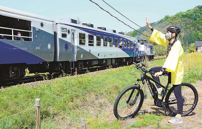 自転車に乗ってトロッコ列車「奥出雲おろち号」に手を振る雲南市観光協会の職員＝雲南市木次町寺領
