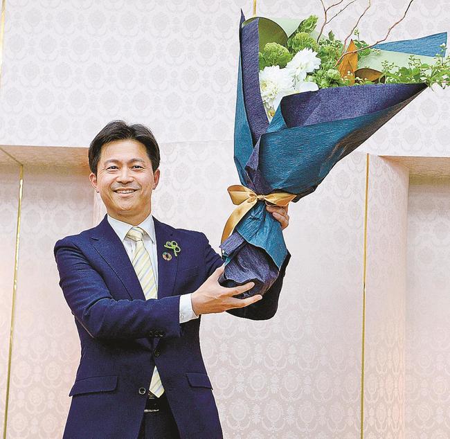 当選を確実にし、花束を掲げる上定昭仁氏＝１８日午後８時５５分、松江市殿町、サンラポーむらくも