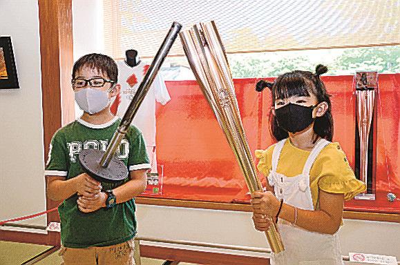 前回の東京五輪聖火リレーのトーチ（左）と今回のトーチを持って記念撮影する来館者＝松江市殿町、松江歴史館