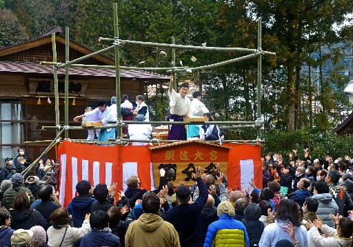 特設やぐらの上からまかれる福豆と福餅の小袋を取り合う参拝者＝出雲市佐田町須佐、須佐神社