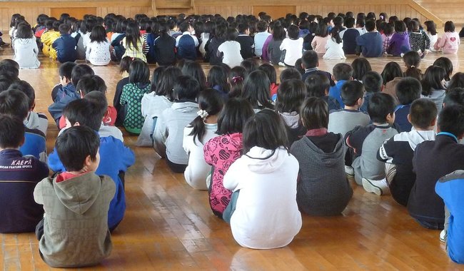 集会で体育館の床に「体育座り」する子どもたち（資料）