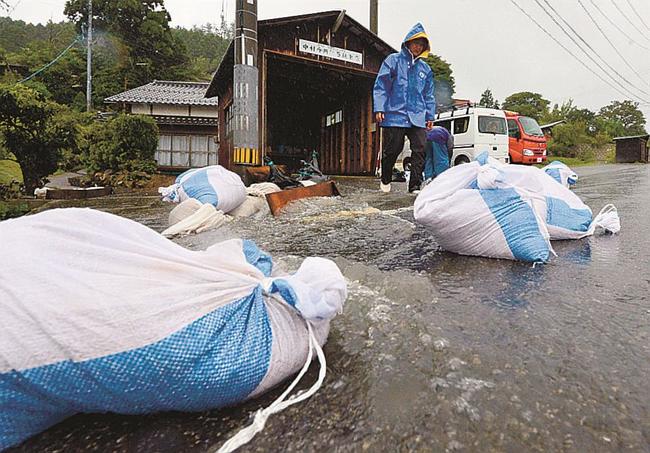 泥水が押し寄せる道路に土のうを並べる人たち＝１７日午後５時３５分、島根県隠岐の島町西村