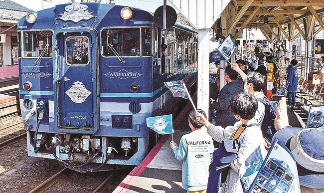 小旗を振り、観光列車「あめつち」を歓迎する沿線住民ら=雲南市木次町里方、JR木次駅