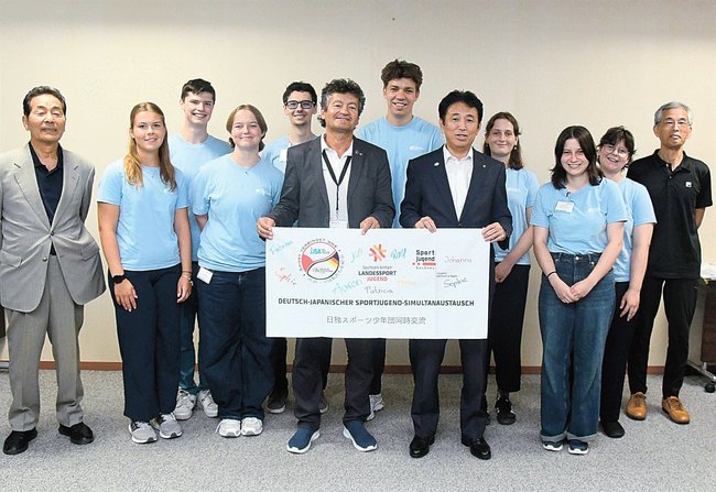 飯塚俊之市長（右から５人目）にメッセージ入りのフラッグを手渡すドイツスポーツ少年団の関係者＝出雲市今市町、市役所