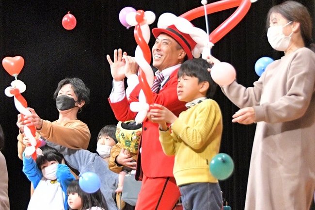 さと原人さん（中央）バルーンアートでステージに立つ親子＝米子市角盤町２丁目、市公会堂