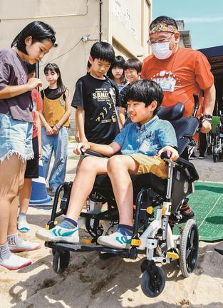 車いすを押してもらいながら、砂場を進む児童＝米子市両三柳、加茂小学校
