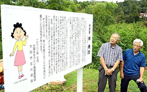 林春生の功績を伝える看板を眺める地域住民＝大田市大屋町