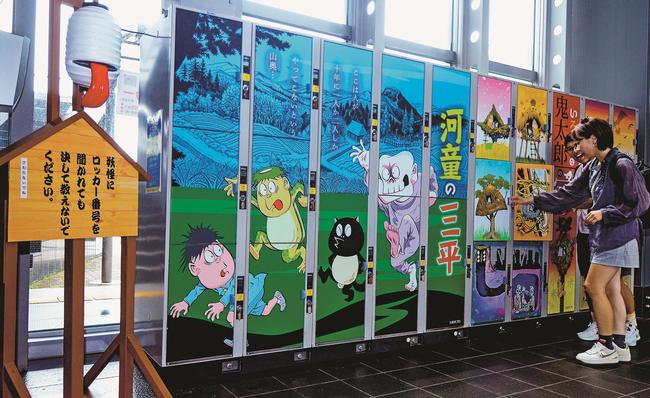 「河童の三平」のラッピングが施されたコインロッカーを見る観光客＝境港市大正町、みなとさかい交流館